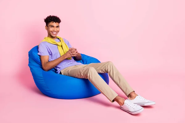 Πλήρες μέγεθος προφίλ πλευρά φωτογραφία του νεαρού χαρούμενα μαύρο άνδρα χαρούμενο θετικό χαμόγελο υπόλοιπο σε καρέκλα φασόλια απομονώνονται σε παστέλ χρώμα φόντο — Φωτογραφία Αρχείου
