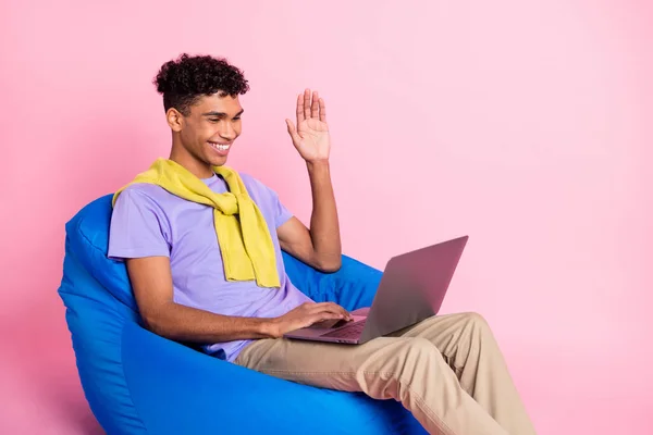 Foto de perfil de un chico moreno optimista agradable hablar portátil usar pantalones de camiseta aislados en el fondo de color rosa —  Fotos de Stock