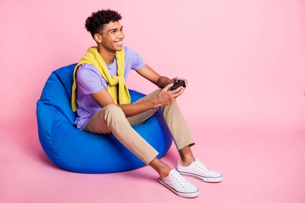 Volledig lichaam profiel zijkant foto van jonge zwarte man gelukkig glimlach spel joystick zitten stoel geïsoleerd over pastel kleur achtergrond — Stockfoto