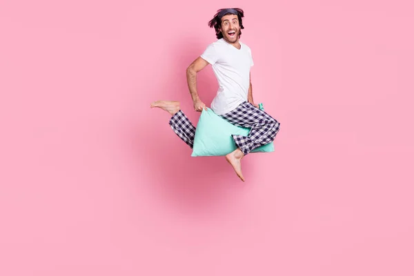 Full size photo of young crazy smiling funky man jumping riding pillow energetic morning isolated on pink color background — Stock Photo, Image