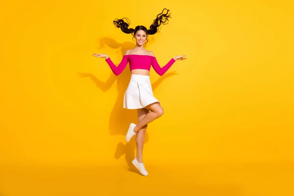 Foto de tamaño completo de optimista encantadora dama morena salto usar falda superior rosa aislado sobre fondo amarillo — Foto de Stock