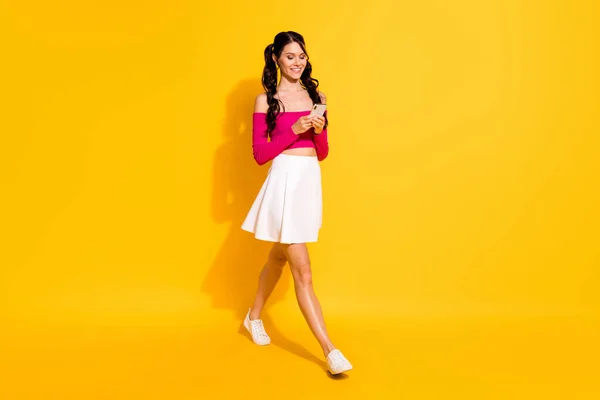 Foto de tamaño completo de optimista encantadora dama morena ir llevar teléfono ropa rosa falda superior aislado sobre fondo amarillo —  Fotos de Stock