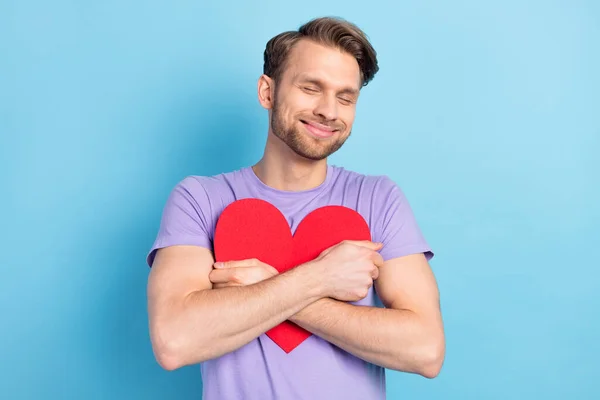 Photo portrait of young man hugging dreamy red heart with closed eyes isolated on pastel blue color background — Stock Photo, Image