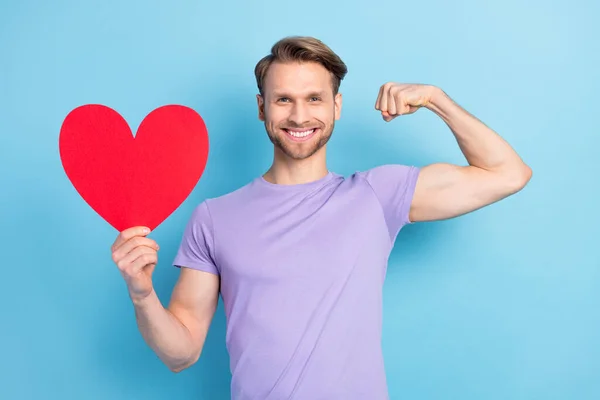 Foto portrét mladého muže ohromen ukazující červené srdce silné biceps izolované na pastelové modré barvy pozadí — Stock fotografie