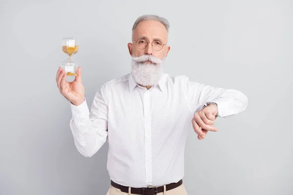 Foto van ernstige kalme oude man dragen bril horloge hold zang uur glas geïsoleerd op grijze kleur achtergrond — Stockfoto