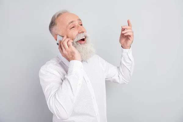 Profiel foto van knappe vrolijke grijze haren oude man praten telefoon dragen witte shirt geïsoleerd op grijze kleur achtergrond — Stockfoto