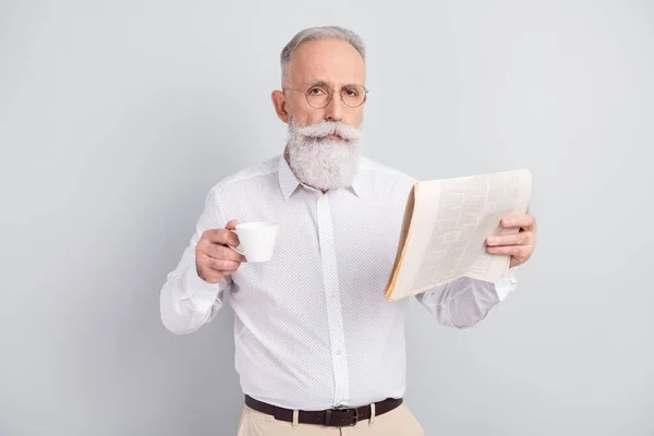 Foto de un hombre serio, viejo, tranquilo, inteligente, imponente, sostiene la taza de periódico de té aislado sobre un fondo de color gris — Foto de Stock