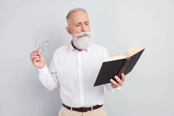 Foto de hombre anciano concentrado centrado leer historia novela libro mantenga gafas aisladas sobre fondo de color gris — Foto de Stock