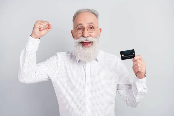 Foto do homem idoso feliz sorriso positivo segurar cartão de crédito alegrar vitória punhos de sucesso mãos isoladas sobre fundo de cor cinza — Fotografia de Stock