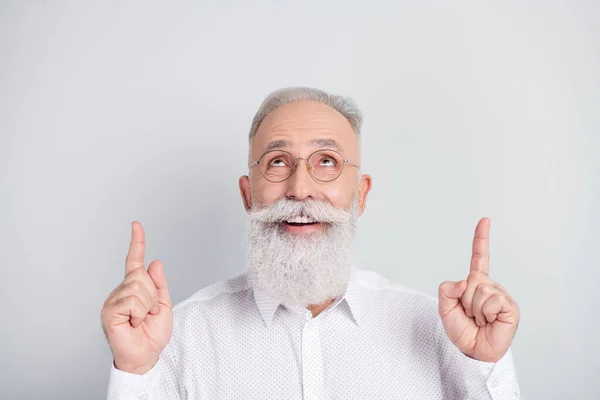 Foto de feliz hombre viejo positivo apuntar los dedos hacia arriba mirar espacio vacío consejo anunciar aislado sobre fondo de color gris — Foto de Stock