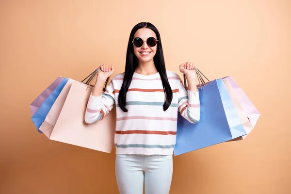 Photo of young beautiful cheerful smiling positive girl in sunglasses hold shopping bags isolated on beige color background — Stock Photo, Image