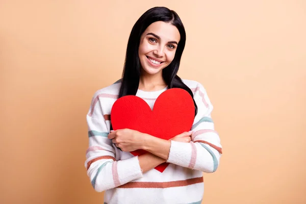 Foto av ung glad flicka glad leende omfamna stora röda papper hjärta Alla hjärtans dag isolerad över beige färg bakgrund — Stockfoto