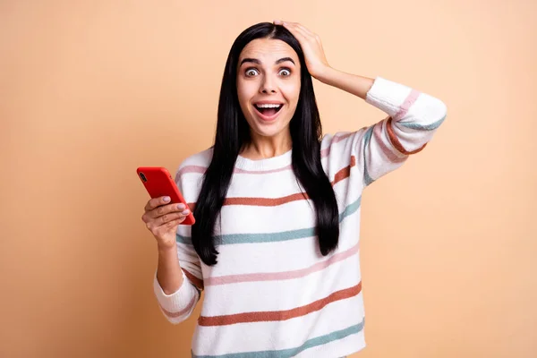 Fénykép a fiatal őrült nő boldog mosoly megdöbbent meglepett használata mobiltelefon kéz érintés fej elszigetelt bézs színű háttér — Stock Fotó