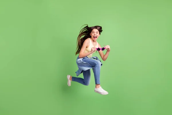 Full size foto van jong gek opgewonden funky meisje springen hold funky zonneglas schreeuwen geïsoleerd op groene kleur achtergrond — Stockfoto