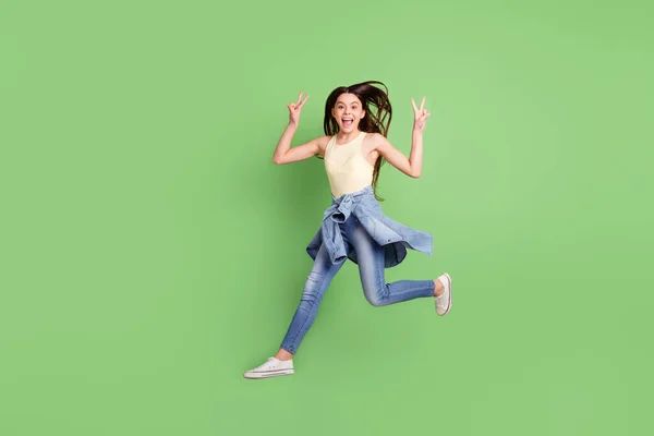 Longitud completa tamaño del cuerpo vista de chica alegre bastante funky saltando caminando mostrando v-signo aislado sobre fondo de color verde brillante —  Fotos de Stock