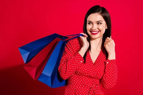 Foto de doce morena senhora segurar sacos olhar espaço vazio desgaste vestido vermelho isolado no fundo de cor vívida — Fotografia de Stock