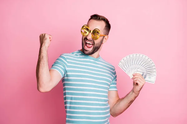 Close-up portrait of nice cheerful guy wearing dollar specs celebrating holding in hands cash budget isolated over pink pastel color background — Stock Photo, Image