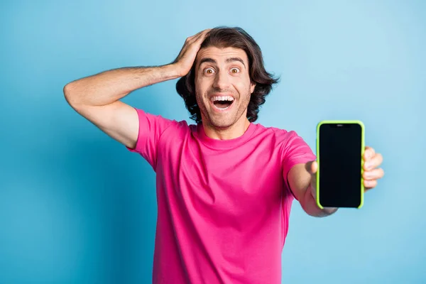 Heyecanlı esmer saçlı adamın fotoğrafı. Cep telefonunu satılık gösteriyor. Kafası boş, mavi arka planda. — Stok fotoğraf