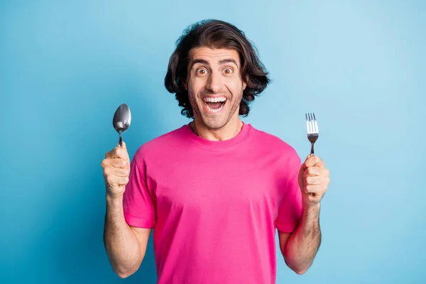 Портрет привлекательного веселого парня, держащего в руках ложку вилки ожидая вкусный обед изолирован на ярко-голубом фоне — стоковое фото