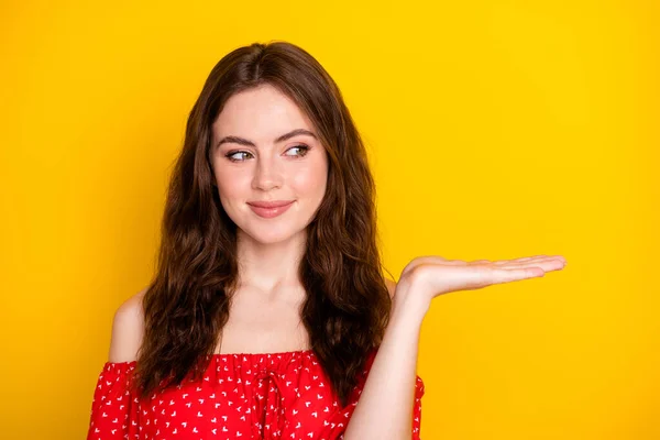 Foto retrato de menina agradável em blusa vermelha curioso manter espaço vazio na palma da mão aconselhando isolado vibrante cor amarela fundo — Fotografia de Stock