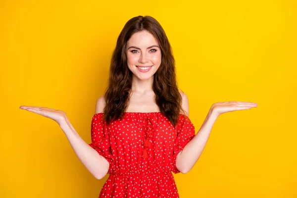 Φωτογραφία πορτρέτο του ωραίο κορίτσι σε κόκκινο φόρεμα συγκρίνοντας κενό χώρο στην παλάμη χαμογελώντας απομονωμένο ζωντανό κίτρινο χρώμα φόντο — Φωτογραφία Αρχείου