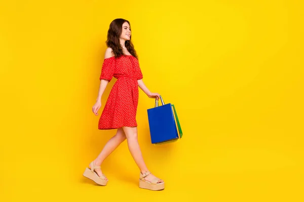 Volledige grootte profiel foto van charmante positieve dame kijken lege ruimte houden tassen geïsoleerd op gele kleur achtergrond — Stockfoto