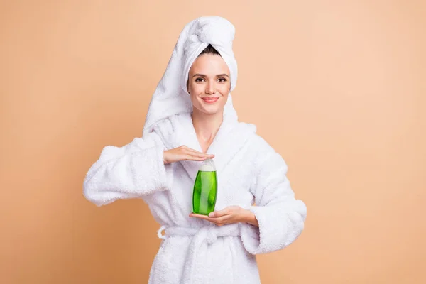 Foto da jovem mulher feliz mostrar xampu garrafa desgaste turbante banheiro roupa isolada no fundo cor bege — Fotografia de Stock