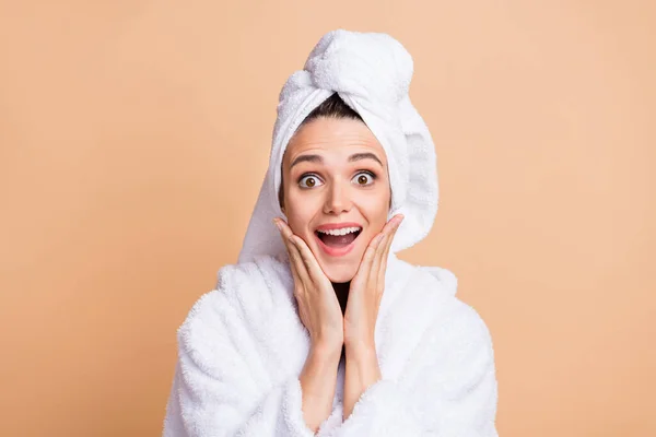 Foto von attraktiven erstaunt junge Frau halten Hände Wangenknochen tragen Bademantel isoliert auf beige Farbhintergrund — Stockfoto