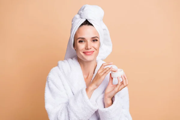 Porträt von hübschen fröhlichen Mädchen tragen Bademantel Anwendung Nachtcreme Produkt isoliert über beige Pastellfarbe Hintergrund — Stockfoto