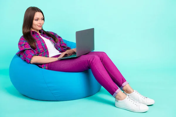 Potret gadis cantik yang terfokus dan ceria yang terbaring di kursi tas menggunakan laptop yang terisolasi di atas latar belakang warna yang cerah — Stok Foto