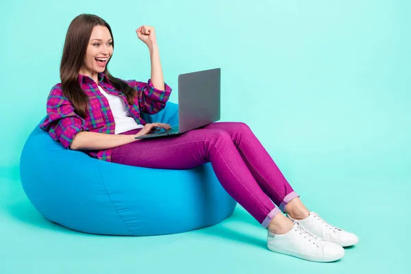 컴퓨터를 사용하여 가방 의자에 누워 밝은 청록색 배경을 놓고 즐겁게 노는 매력적 인 명랑 한 소녀의 모습 — 스톡 사진