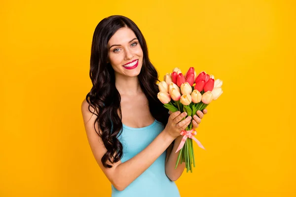 Foto de la encantadora joven dama mantenga manojo tulipanes sonrisa dentada desgaste vestido azul aislado color amarillo fondo — Foto de Stock