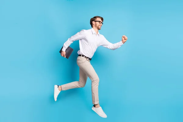 Повнорозмірний вигляд тіла привабливого веселого чоловіка, який стрибає з ноутбуком, ізольований на яскраво-синьому кольоровому фоні — стокове фото