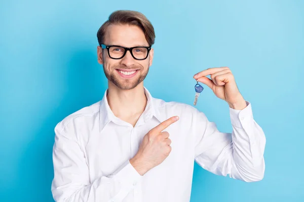 Portrait of attractive cheerful man holding in hand demonstrating key realestate ownership isolated over bright blue color background — Stock Photo, Image