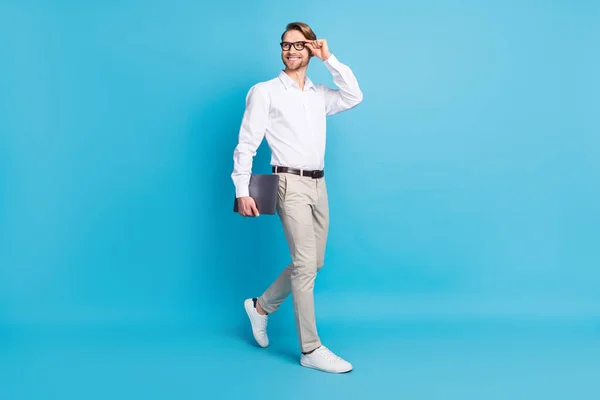 Full body foto aantrekkelijk positief jonge man lopen glimlach zakenman kijken leeg ruimte houden laptop geïsoleerd op blauwe kleur achtergrond — Stockfoto