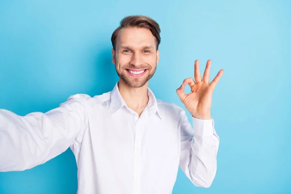 Foto av glad positiv glad ung man gör selfie show okej tecken leende isolerad på blå färg bakgrund — Stockfoto