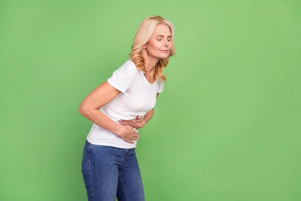 Foto de perfil de señora enferma rubia envejecida sostiene el vientre usar camiseta blanca aislada sobre fondo de color verde pastel — Foto de Stock