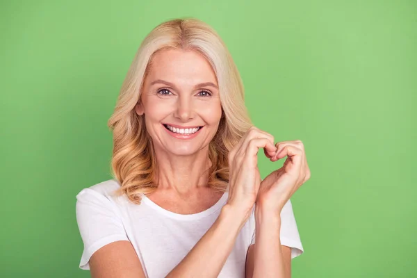 Foto porträtt äldre kvinna visar hjärtformade tecken leende isolerad på pastell grön färg bakgrund — Stockfoto