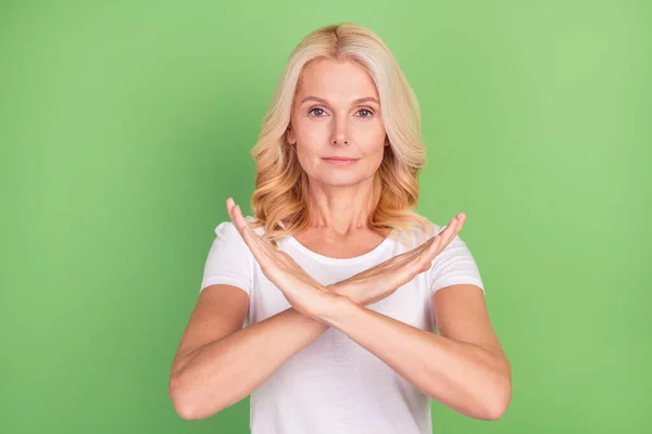 Zdjęcie ścisłe blondynka starsza pani pokazać zakazać znak nosić biały t-shirt izolowane na pastelowy zielony kolor tła — Zdjęcie stockowe