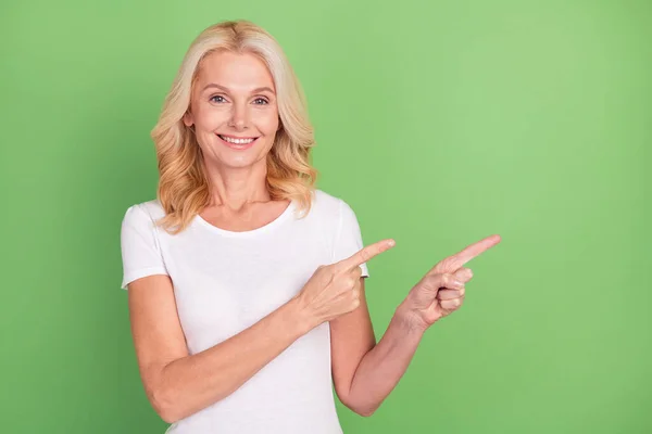 Zdjęcie optymistycznej blondynki w wieku pani punkt puste miejsce nosić biały t-shirt odizolowany na pastelowym tle zielony kolor — Zdjęcie stockowe