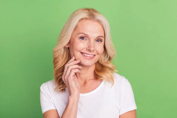 Foto retrato mulher mais velha tocando rosto sorrindo em roupa casual isolado pastel cor verde fundo — Fotografia de Stock