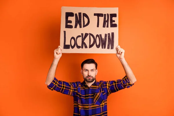 Portrait of handsome guy hands hold end the lockdown poster above head isolated on orange color background — Stock Photo, Image