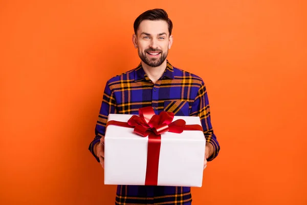 Foto de manos de hombre joven satisfecho sostiene giftbox radiante sonrisa mirada cámara aislada sobre fondo de color naranja —  Fotos de Stock