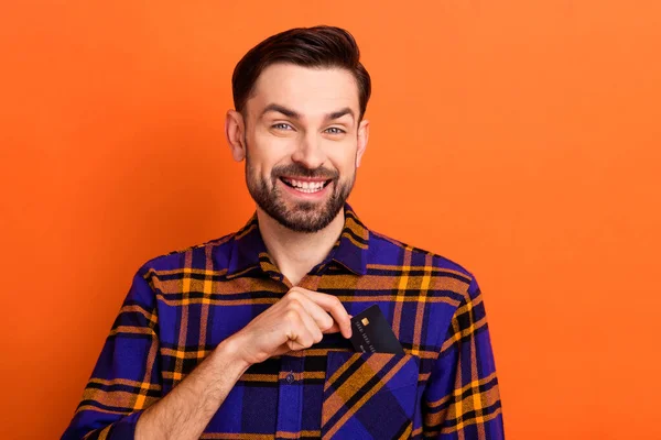 Portret van positieve persoon arm te nemen bankkaart uit zak tand glimlach geïsoleerd op oranje kleur achtergrond — Stockfoto