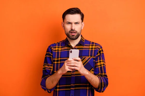 令人印象深刻的不满意的男人的画像，手拿着用橙色背景隔开的手机盯着相机 — 图库照片