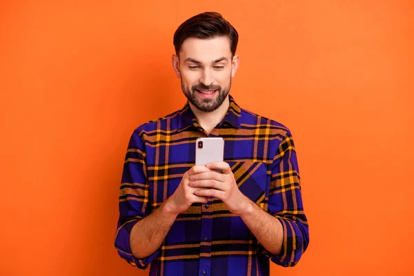照片上年轻英俊的男人开心而积极的笑着看浏览智能手机聊天室类型的Sms隔离在橙色背景下 — 图库照片