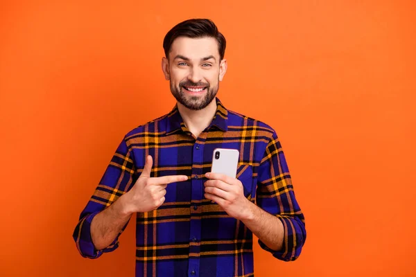 若い男の写真幸せな笑顔は、指のスマートフォンの広告プロモーションの選択は、オレンジの色の背景に孤立をお勧めします示す — ストック写真