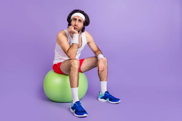 Full size photo of young unhappy upset sad athlete man in glasses sit ball cant exercise isolated on violet color background — Stock Photo, Image