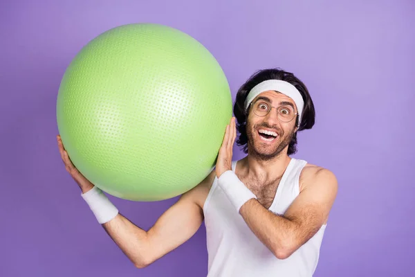 Foto von optimistischen brünetten Kerl halten Ball tragen Brille weiß singlet Haarband isoliert auf lila Hintergrund — Stockfoto