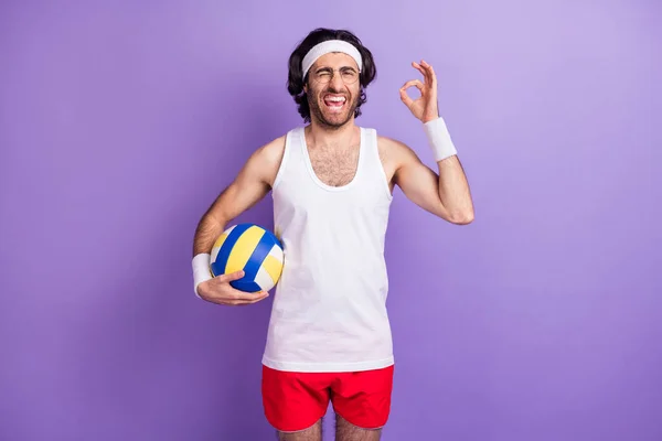 Photo of optimistic brunette guy show okey hold ball wear spectacles white singlet isolated on lilac color background — Stock Photo, Image